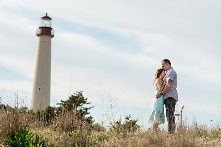 A woman rests her head on her fiance's chest in front of the cape may lighthouse.